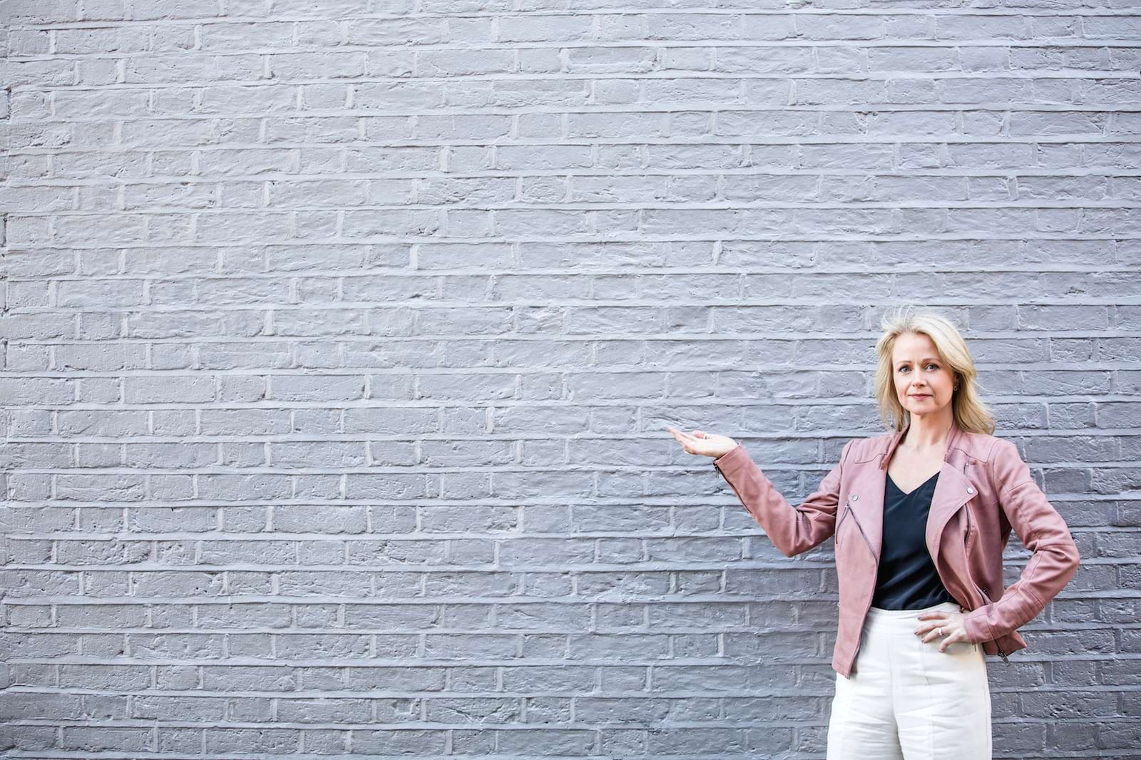 women pointing sidways on the right hand side of a brick wall with lots of negative space 